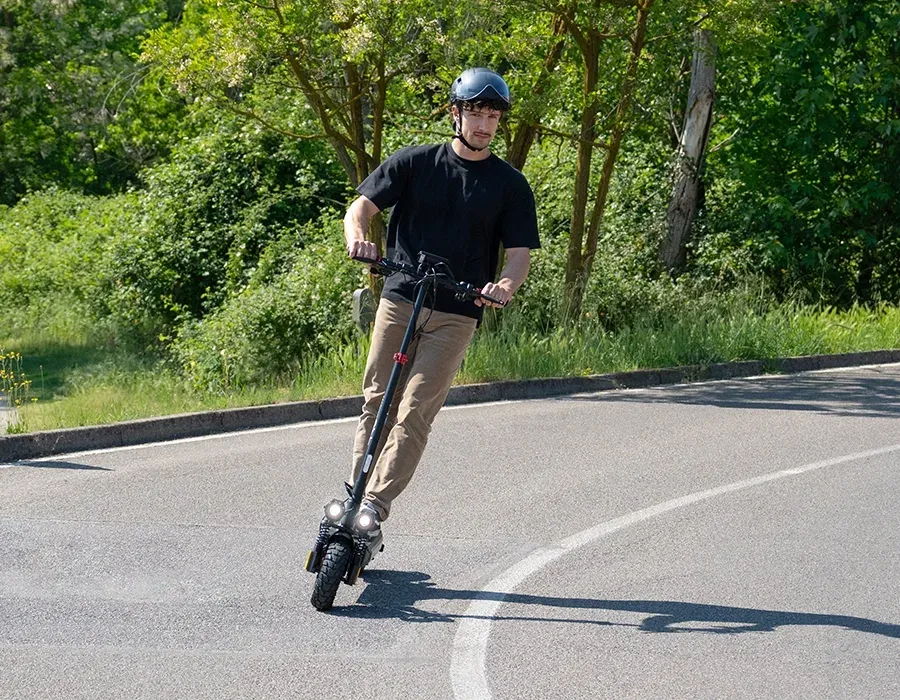 Un homme casqué négocie un virage sur une route bordée d'arbres avec l'Urbanglide Ecross Go