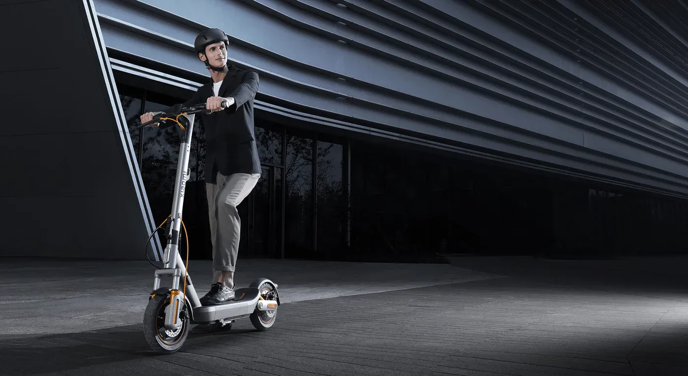 Un homme casqué roule sur une Xiaomi Electric Scooter 6 Max devant un bâtiment moderne